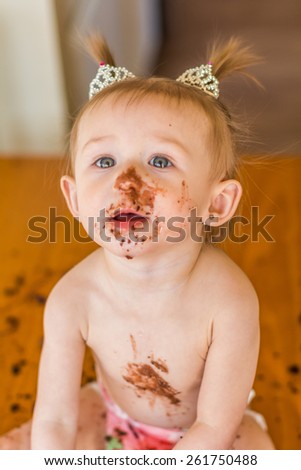 Baby girl with pigtails celebrating her first birthday with chocolate cake. Photo taken inside a home in Reno, Nevada, USA using natural window light.