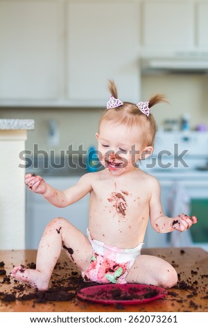 Baby girl with pigtails celebrating her first birthday with a chocolate cake. Photo taken in a home in Reno, Nevada, USA with natural window light.