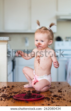Baby girl with pigtails celebrating her first birthday with a messy chocolate cake. Photos taken inside a home in Reno, Nevada, USA using natural window.