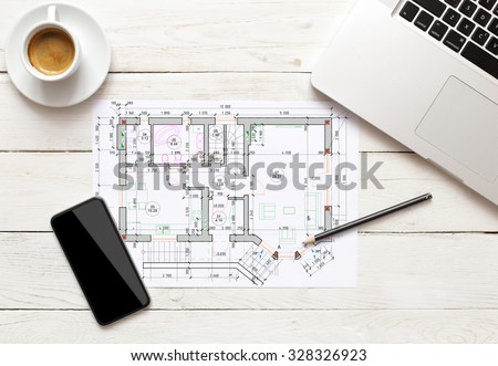 building plan on office table with notepad, computer and coffee cup.