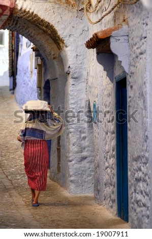 moroccan woman carrying bread on her head in the narrow streets of blue town of chechaouen