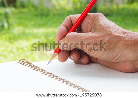 Old man right hand writing with red pencil on green background