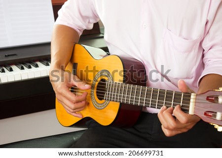 Closeup man\'s hands playing classic guitar with piano background.