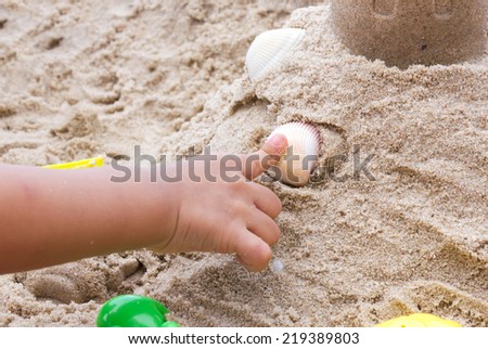Closeup Children\'s finger point shell. Children plays toy on sand.