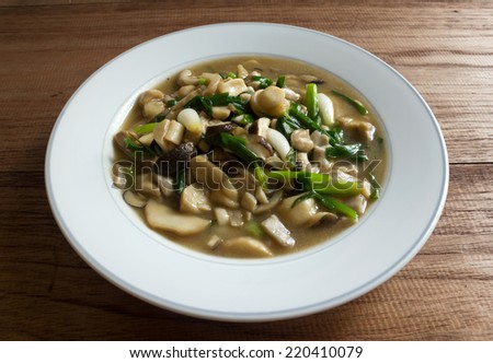 Stir-fried mushrooms and green onion, vegetarian food. On white plate and wooden table.