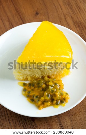 Passion fruit cake with fruit on white plate. Wood background.