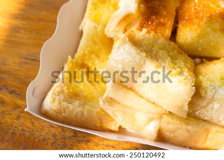 Closeup grilled bread with butter and sugar topping in a white paper plate. On wooden table.