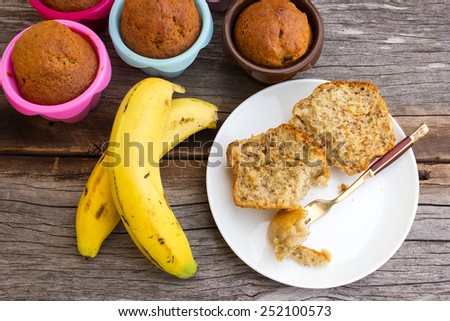 Banana cup cake in a white plate. With banana cup cake in colorful baking pan (silicone) and banana are background.  On wooden table. Top view.