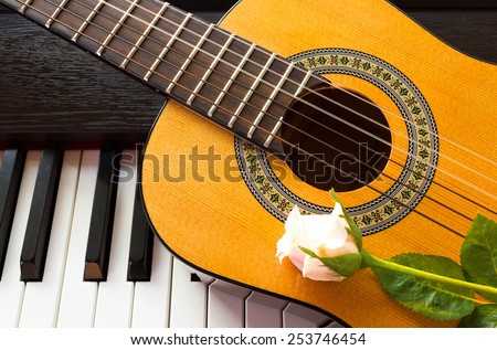 Pink rose on guitar and piano keyboard. Selected focus on guitar.
