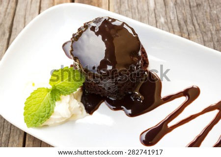 Chocolate cake with whipping cream on white plate. Over wooden table. Decorate with chocolate sauce and mint leaf.