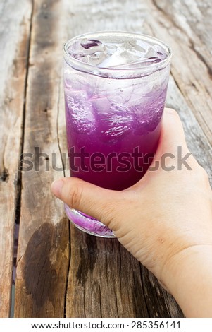 Woman\'s hand taking a glass of Butterfly pea and lemon juice  on wooden table. Herb drink for refreshment.