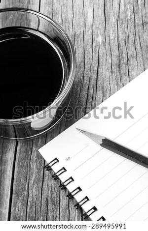 Black coffee and an empty notebook with pencil on wooden table. Black and white theme. Concept background.