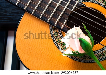 Closeup guitar with pink rose on piano keyboard. Select focus on neck of guitar. Vintage style and high contrast color tone.