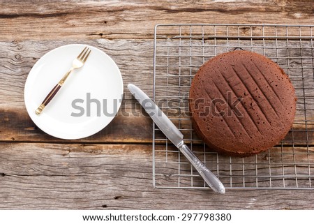Chocolate cake on baking rack with white plate and knife. Over wooden table. Top view.