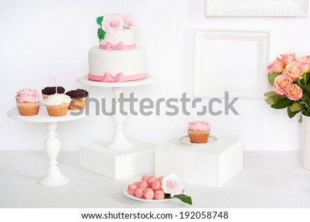 Cake decorated with roses and bows with cupcakes and macaroons standing on a table
