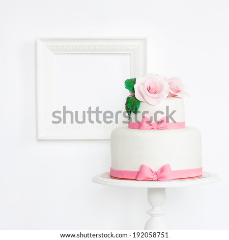 Cake decorated with mastic roses and pink bows on stand with frame on white background