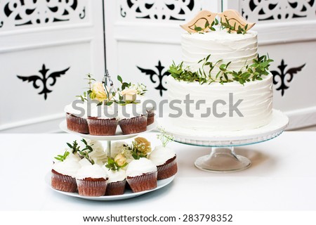 Wedding cupcakes and cake decorated with flowers on white stand as candy bar