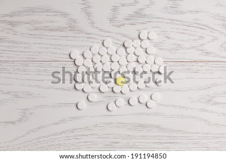 Yellow pill among white pills on wooden table