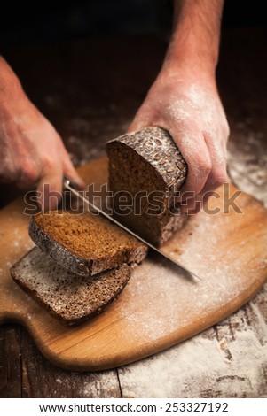 Male hands slicing fresh bread on wood table