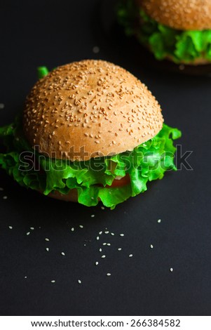 Homemade hamburger with fresh green lettuce, tomato and red onion on black background