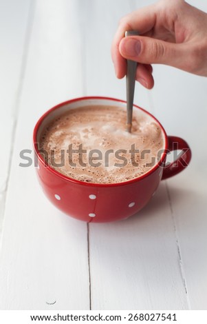 Woman hand holding spoon in cup of chocolate in red cup