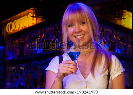 portrait of a pretty blond girl smiling and drinking in a bar