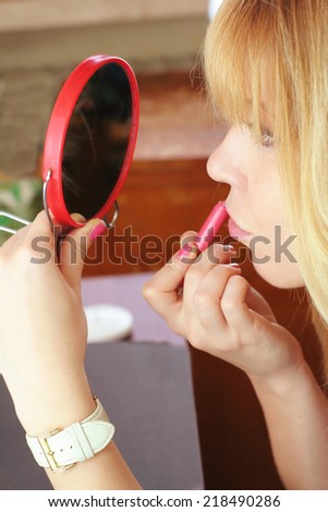 a cute blonde girl doing make up with a mirror using lipstick