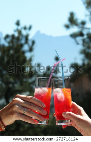 saying cheers 2 peoples hands holding colorful chilled cocktails toasting under bright sunshine portrait image