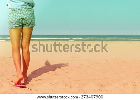 a close up partial shot on a girl's legs wearing shorts and beach slippers walking towards the sea on the beach on a hot summer day:  retro filtered image