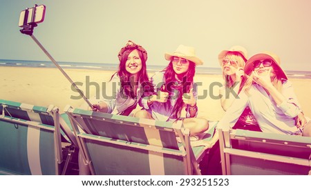 4 girls interracial best friends on beach taking self portrait using a selfie-stick. Happy girls smiling and making funny faces and mustache with hair retro vintage filter and custom white balanced