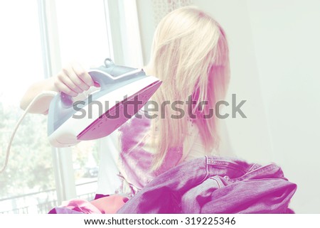 young woman ironing clothes doing domestic work and laundry. focus on clothes and iron    woman\'s hair has motion blur. Iron image is retro look filtered with pinkish color tones.