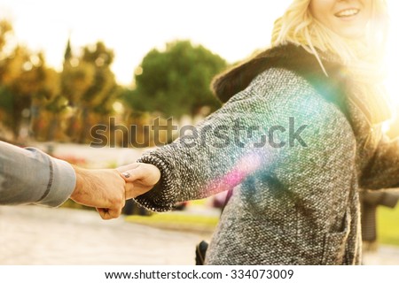 follow me - happy young hipster woman pulling guy\'s hand - hand in hand walking on a bright sunny day in autumn - concept of carefree modern life - focus on hands, sunburst and lens glare effects