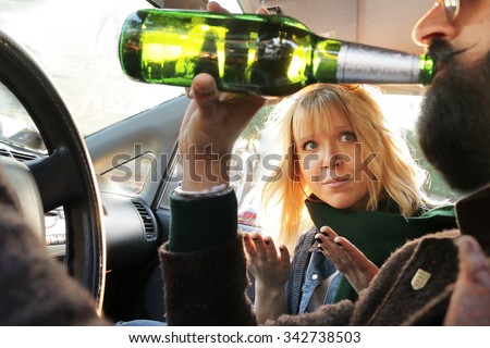 drink and drive - man drinks off a bottle of beer while driving car and passenger woman looks worried and disagree. concept of alcohol, dangerous driving