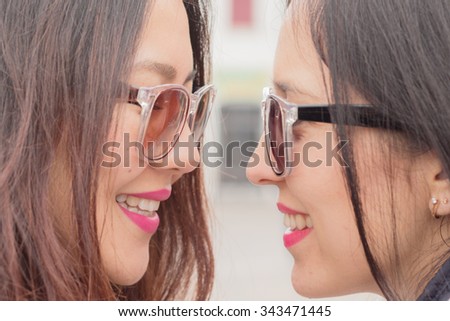 best friends - 2 beautiful trendy multi ethnic girls with smiling faces closely looking at their eyes, friendship fun happiness and playful attitude concept