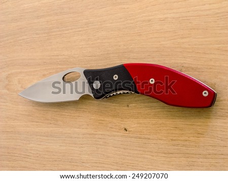 Folding pocket knife with red handle on wooden background