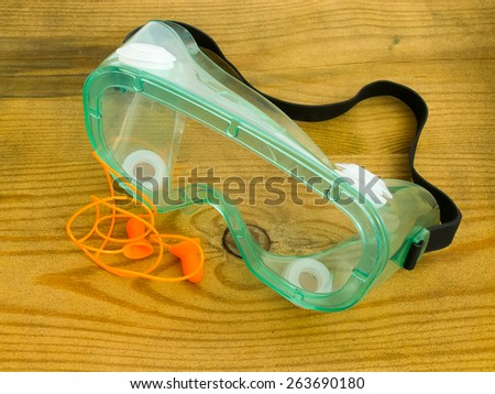 Protective eyeglasses and ear plugs with cord against a wooden background