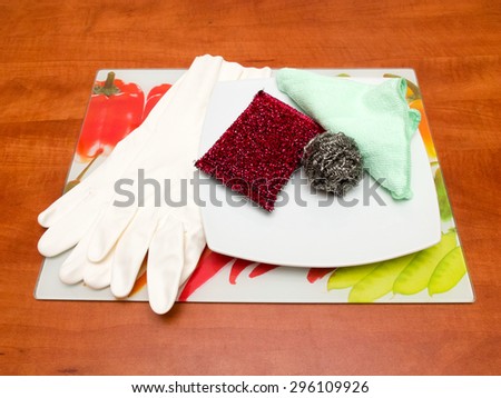 Dish washing sponge, dishcloth, rubber gloves, scrub pad, plate and colored tray on a table.
