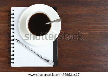 Cup of coffee, pen and opened notepad on desk. Top view