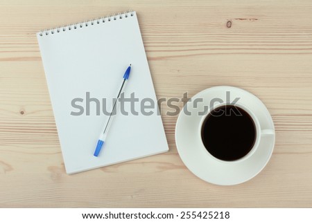 Cup of coffee, pen and opened notepad on desk. Top view