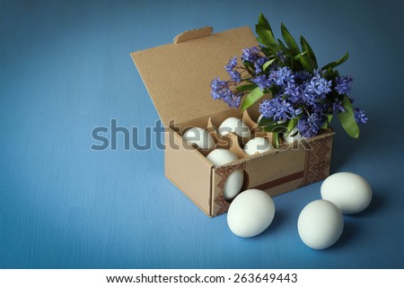 White chicken eggs in an egg box with flowers (Scilla) on a blue wooden background