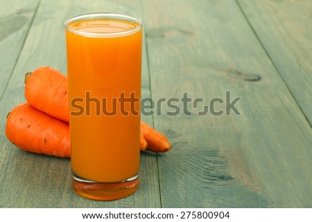 Glass of carrot juice and fresh carrots on wooden background