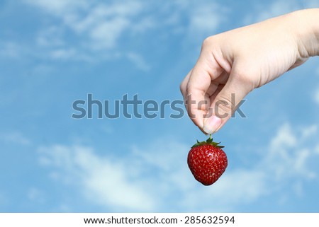 Fresh strawberries in hand against the sky