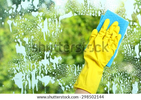 Hand in a yellow glove  wiping soap window with napkin  on the background of trees