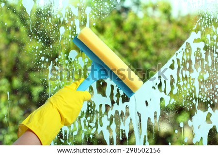 Hand in a yellow glove with special tool washes the soap window on the background of trees