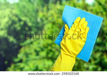 Hand in a yellow glove  wiping  window with napkin  on the background of trees