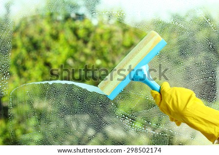 Hand in a yellow glove with special tool washes the soap window on the background of trees