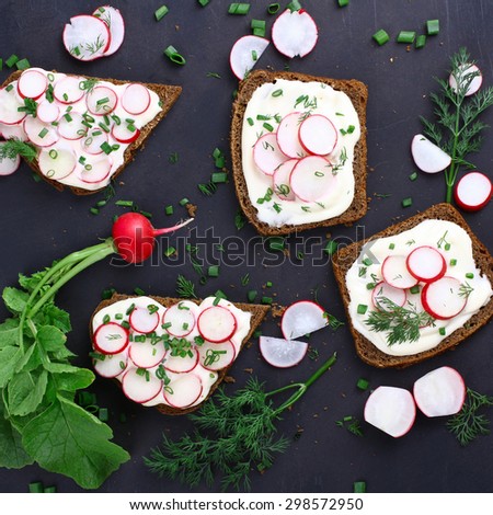 Four sandwiches with sour cream, onions and radishes and sliced radish on a isolated  black background