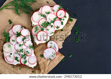 Two sandwiches with sour cream, onions and radishes and dill on a package on a isolated  black background
