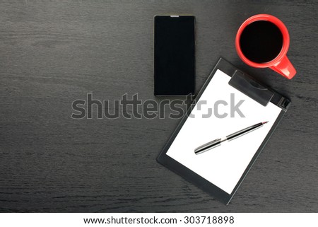 black background, red cup, phone, paper holder, pen