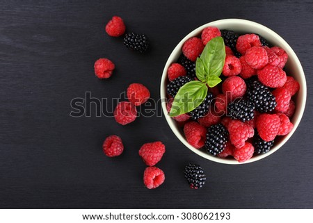raspberries and blackberries in a bowl black background